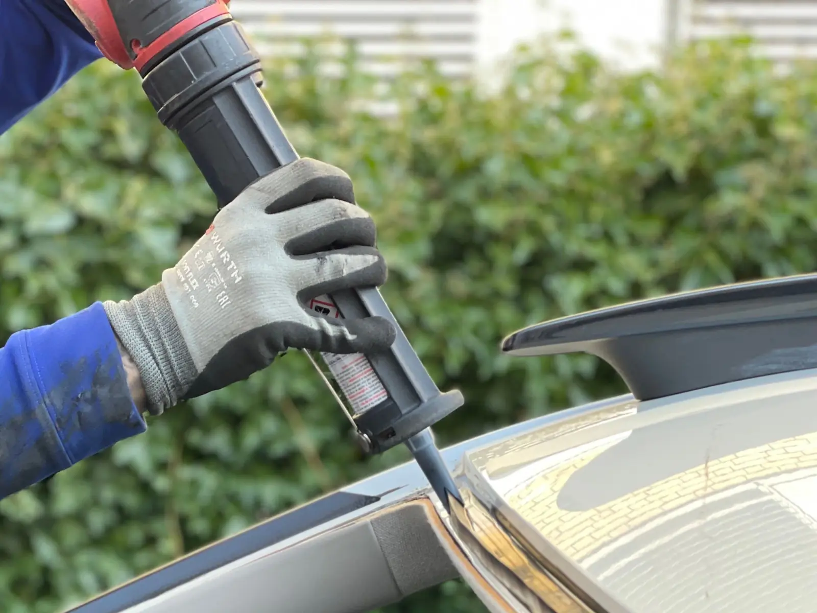 A technician in work gloves running adhesive along the edge of a car windshield